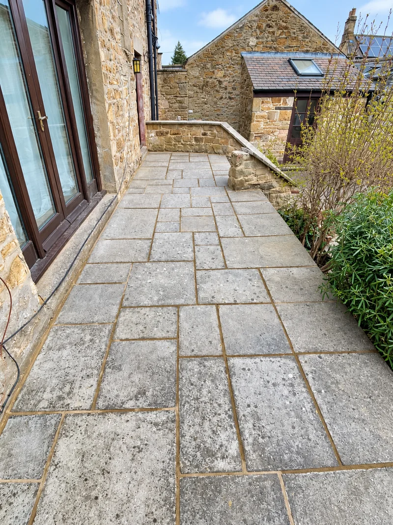 Repointed joints between stone paving slabs beside a stone house; photo enhanced
